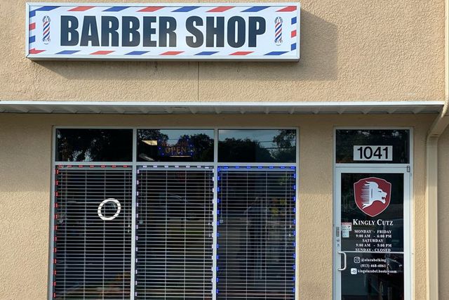 Kingly Cutz Barbershop exterior at twilight, warm glowing lights inside, modern glass facade, Tampa Florida, premium barbershop storefront